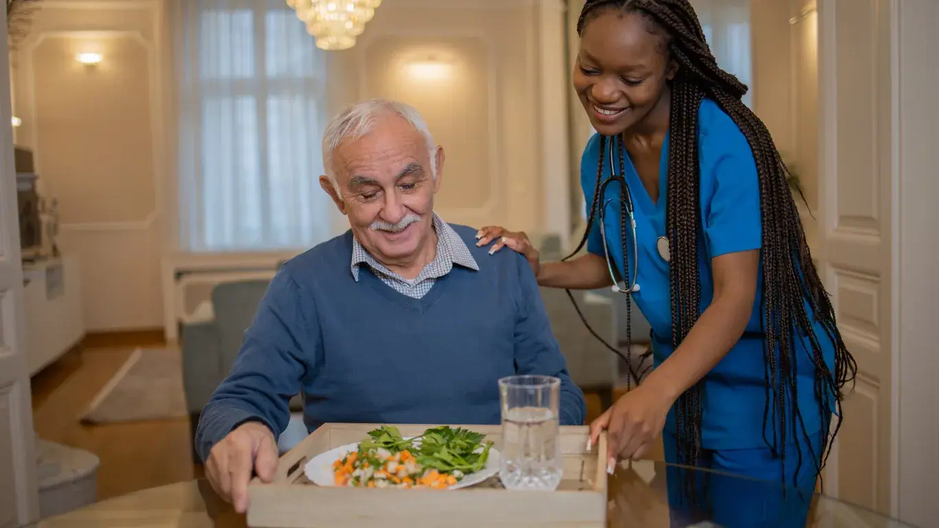 A carer serving a healthy meal to an elderly man at his dining table