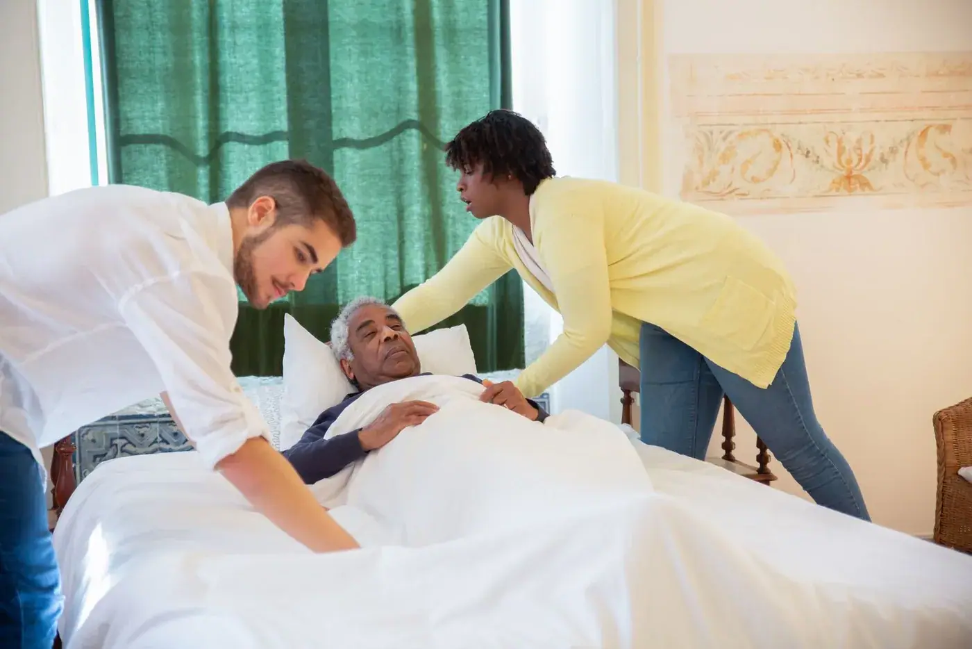 Two carers settling an elderly man into bed
