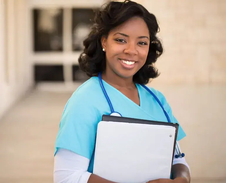 A smiling carer in blue scrubs holding a care folder