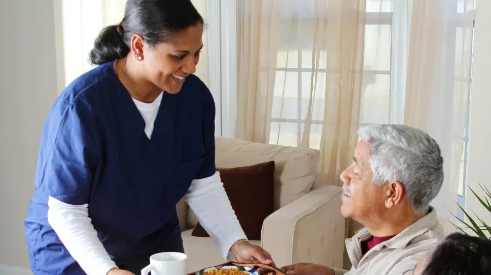 A carer bringing a tray of food and tea to an elderly man